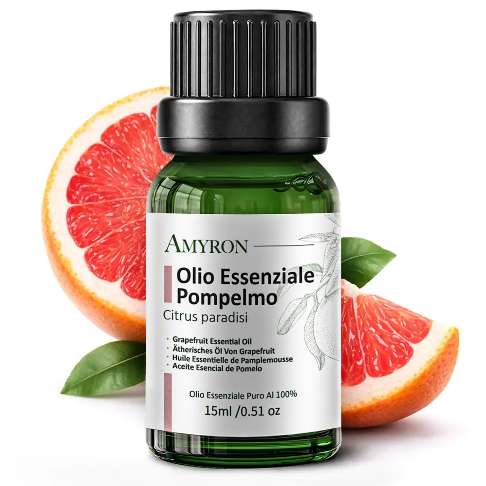 Flacone AMYRON di olio essenziale di pompelmo 15 ml davanti a pompelmi rosa tagliati